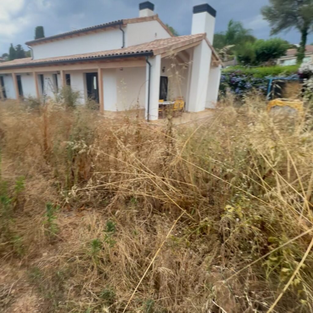 Jardín invadido por maleza seca alta junto a una casa, antes de una limpieza de recuperación en el Tarragonés